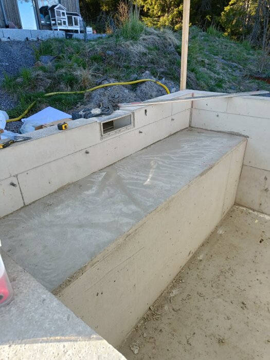 Betongkonstruktion med former borttagna, möjlig framtida avdelare i slänt. Omgiven av byggutrustning och natur.