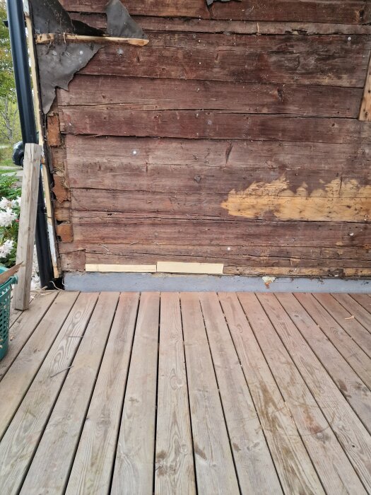 Riven träpanel på husgavel med synlig lagning och ny brädfodring ovanpå trädäck.