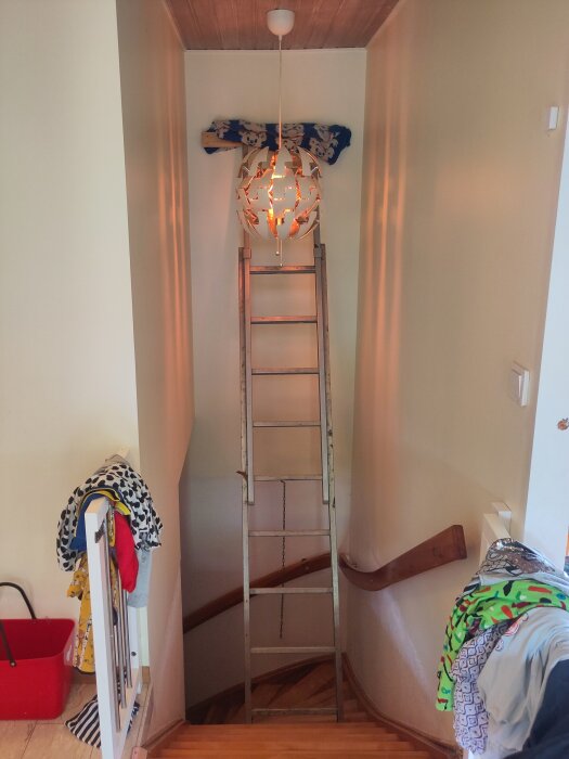 En nyinstallerad taklampa med ett unikt mönster lyser över en trappa. Stege placerad under lampan för att underlätta installationen.