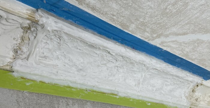 Bild av en trasig gipsstukatur täckt med silikonform, omgiven av blå och grön tejp som del av renoveringsprojektet.