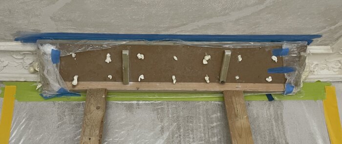 Gjutform för stuckatur tillverkad av trä, plast och expanderande PU-skum, fäst vid taket för provgjutning.