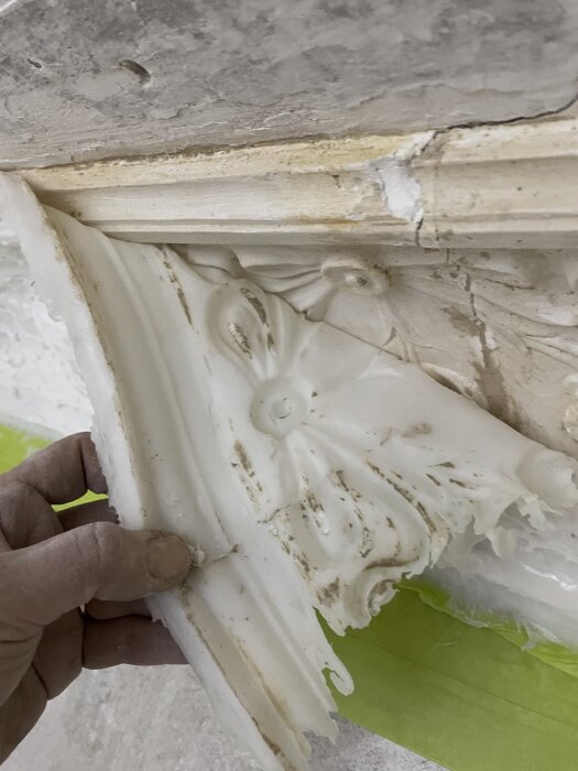 Hand håller en silikonform av en ornamenterad gipsstukatur för att reparera en skadad taklist.