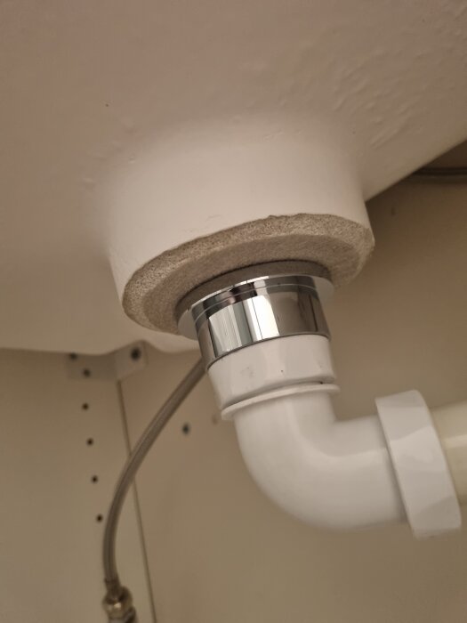 Vitt rör under vask kopplat till avloppsledningen, synliga anslutningar och packningar.