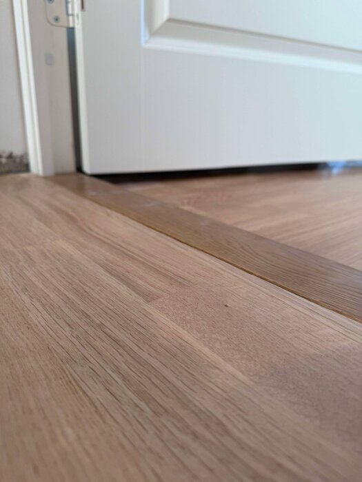 Ny dörrkarm med tröskel i nivå med golvet, synlig springa mellan tröskeln och parkett på grund av ojämnhet i golvet.