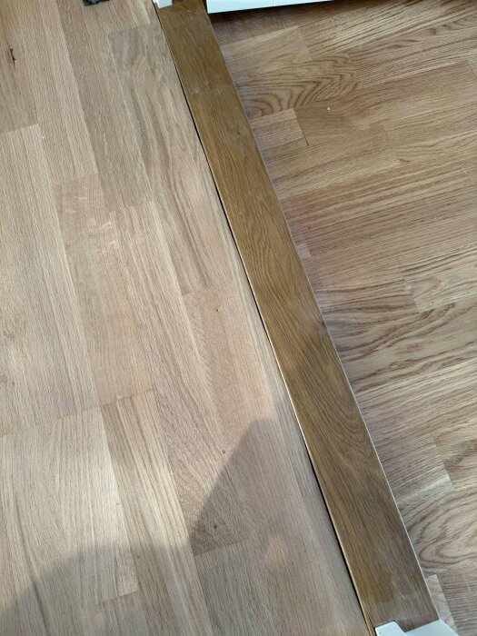 Tröskel i trä i samma höjd som parkettgolv med en synlig springa mellan tröskeln och golvet, som inte ligger helt rakt.