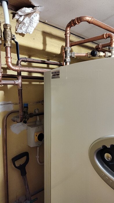 Värmesystem med rör och ventiler, inklusive en blå kran, används för justering av vattenflöde och tryck.