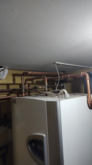 Värmesystem med rör och ventiler, inklusive en blå kran på en vit maskin, i ett utrymme med lågt tryckproblem.