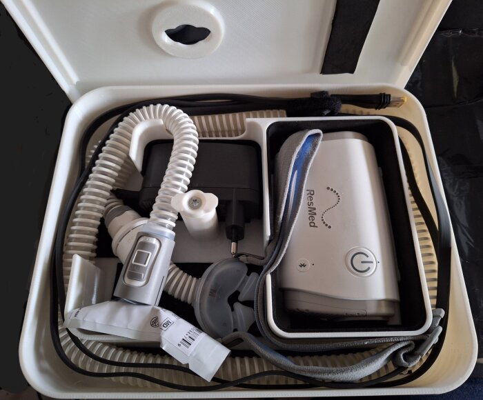 Kompakt resefodral med CPAP-maskin från ResMed, slangar och tillbehör för snarkbehandling.