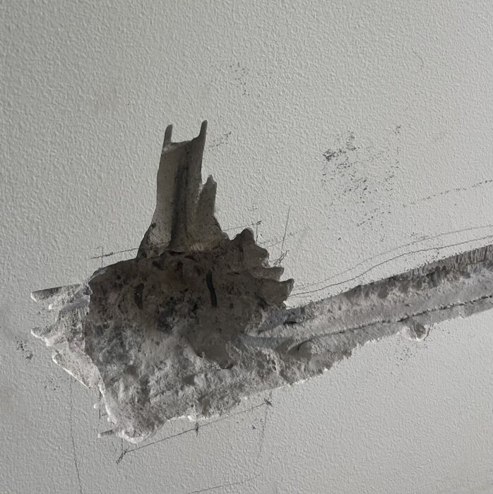 Ett hål och en skåra i en betongvägg, förberett för elinstallation med synliga stenmönster och ojämn kant.