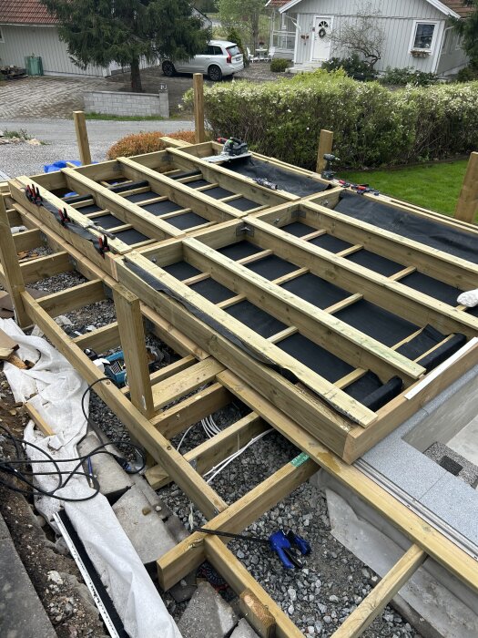 Trästomme av pooltak med EPDM-duk, sett ovanifrån. Verktyg och skenor synliga runt bygget. Hus och grönska i bakgrunden.