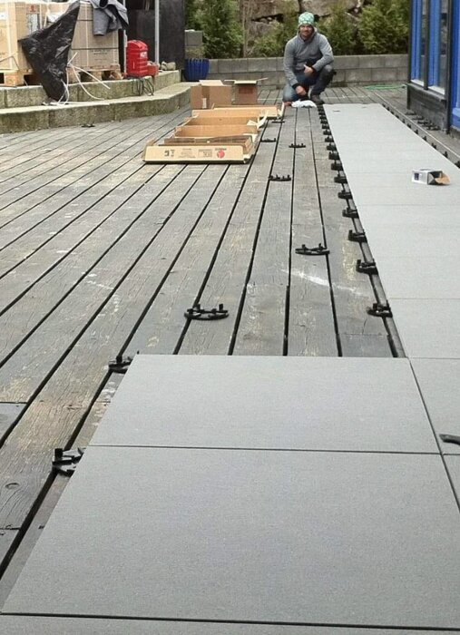 Person monterar stenplattor på en trätrall; kartonger och verktyg ligger runtomkring.