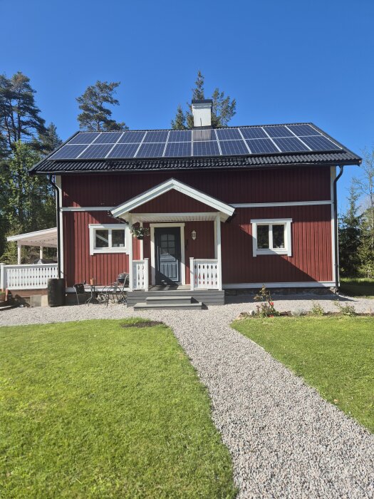Rött hus med vita knutar och solpaneler på taket, grusgång leder fram till verandan.