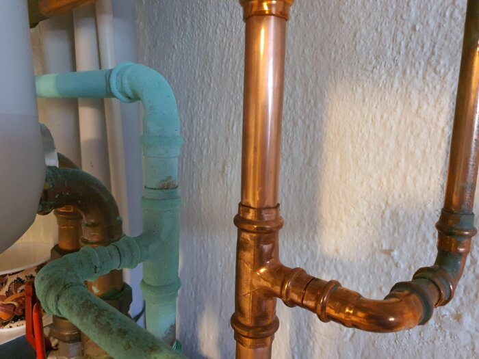 Kopparrör i ett rum, några är gröna av ärg medan andra är opåverkade. Rören är kopplade till en värmeväxlare för fjärrvärme.