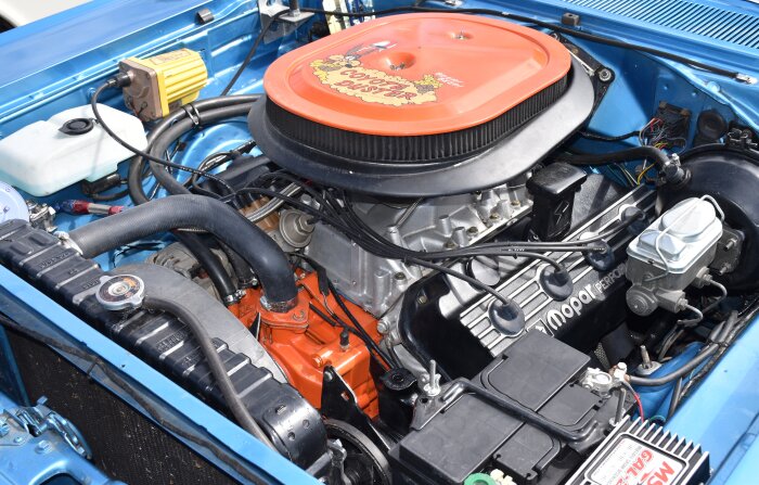 Motor från en bil med orange ventilkåpa och texten "Mopar Performance", fotograferad under en huva i en blå bil i Trollhättan.