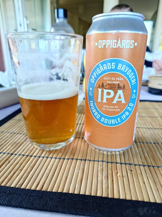 En halvfull ölglas med en burk Oppigårds Thurbo Double IPA 2.0 på en bambumatta.