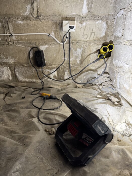 Eluttag med kablar och verktyg på betongvägg i krypgrund. Verktyg ligger på plastskiva, installation för tomatodling.