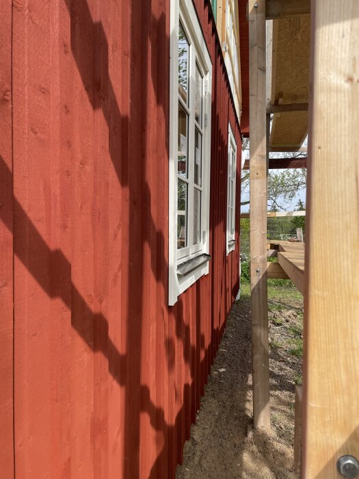 Röd panelvägg med vita fönster, del av ett byggprojekt; skuggor från ställning på väggen.