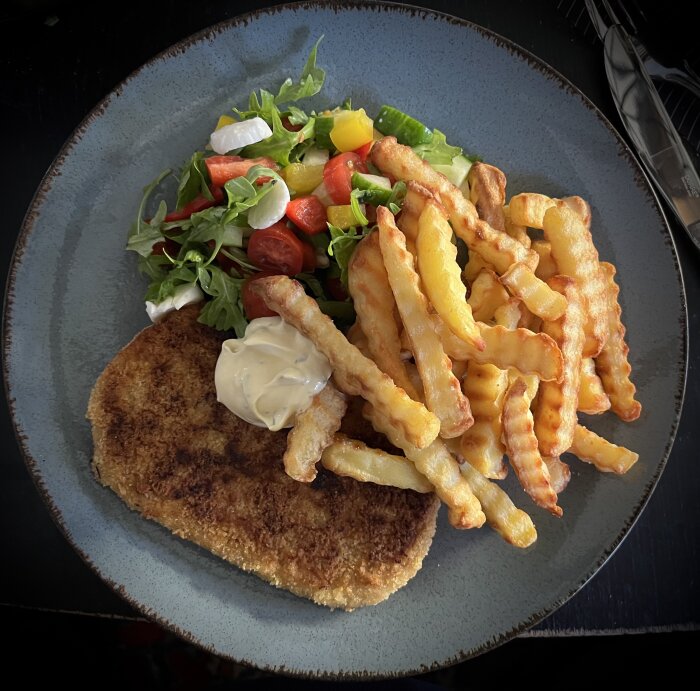 Tallrik med köpescnitzel, krispiga pommes frites, färgglad sallad och en klick bearnaisesås.