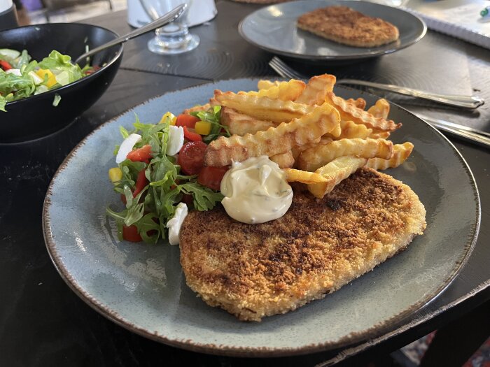 Köpescnitzel med pommes frites, sallad och bearnaisesås på en tallrik.