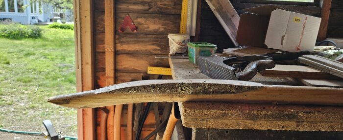 Brutet spadskaft lagas med stumfog och ekbit i verkstad fylld med verktyg och träbitar, för att förstärka och återanvända spaden.