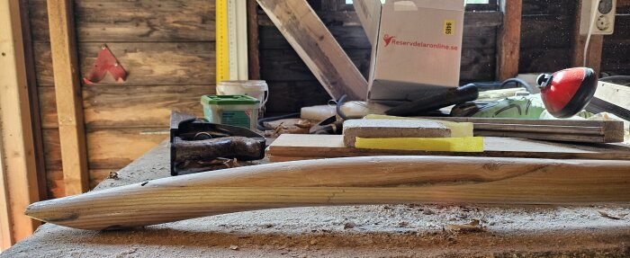 Arbetsbänk i snickarverkstad med en träskaftsspade under reparation, omgivna av verktyg och träspån.