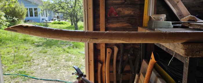 Reparerat och förstärkt skaft av en spade, smält glasfiber runt lagad sektion, verkstadsmiljö med grönskande trädgård i bakgrunden.