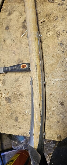 En reparerad och förstärkt spade med trähandtag och metallblad, liggande på ett slitet arbetsbord, bredvid en Bacho kniv.