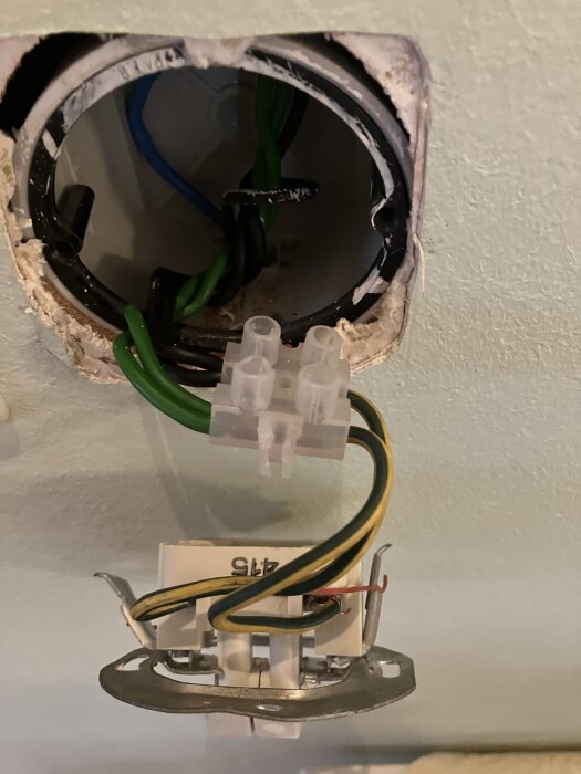 Elektrisk koppling med grön/gul kabel och kronbrytare synliga i en väggöppning; felaktigt seriekopplade brytare.