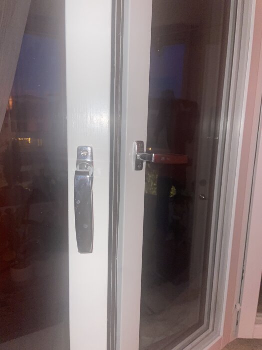 Två olika fönsterhandtag på en vit fönsterkarm, ett med låspigg och ett utan, fotograferade inomhus med mörkt utomhus bakgrund.