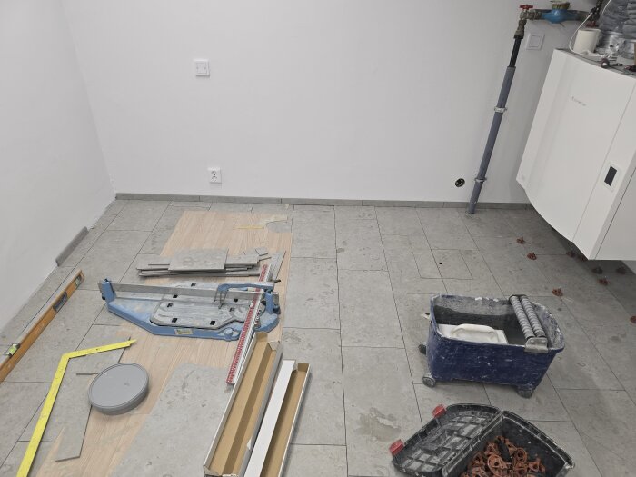 Nyfixerat golv med verktygslådor, brickor och plattor i ett renoveringsprojekt för ett maskinrum. Ljusa väggar och golvplattor, arbete pågår.
