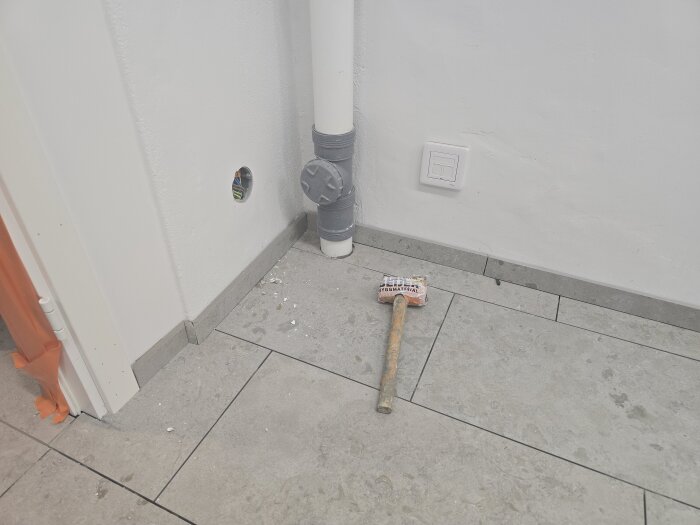 Verktyg och byggmaterial ligger på golvet framför en vägg med eluttag och kabeldosor i ett rum under renovering.