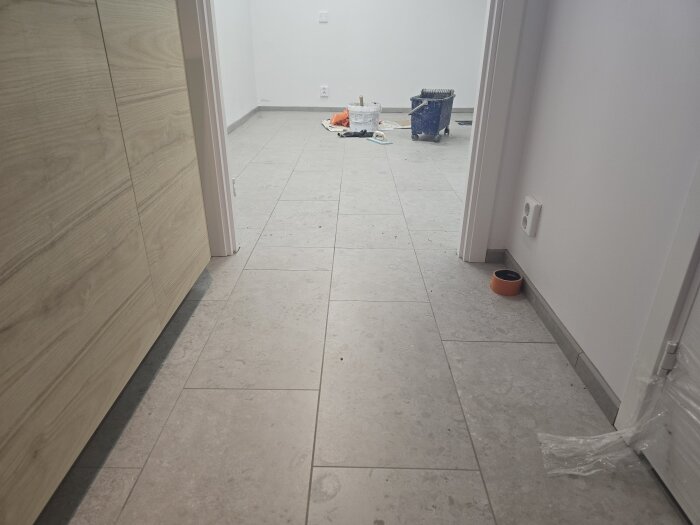 Nyrenoverat rum med grå klinkergolv och plåtlister. Verktyg och material synliga i bakgrunden, samt tomma eldosor på väggarna.