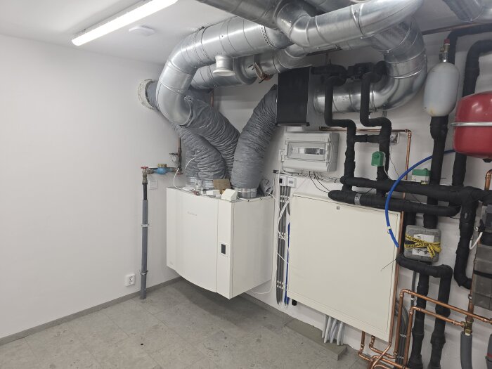 Maskinrum med ventilationsrör, VVS-installationer och takbelysning. Lysrör ger starkt ljus utan bländning i det fönsterlösa rummet.