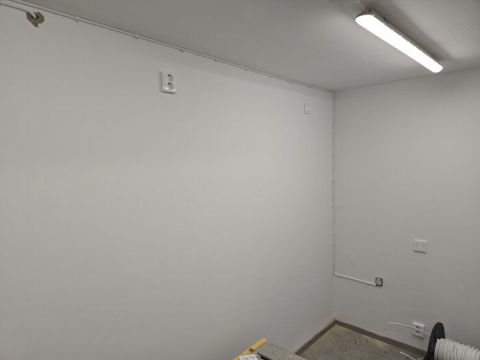 Vitt rum med nyinstallerade eluttag och kablar längs väggen, ljusrör i taket och en rulle vit kabel på golvet.