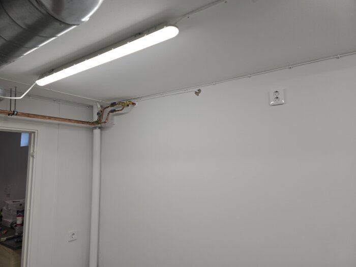 Elinstallation i rum med nytt eluttag på väggen, synliga rörledningar och lysrör i taket.