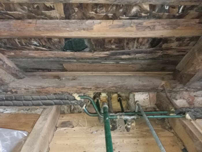 Bild på en gammal rördragning i ett övervåningsgolv med synliga ledningar och träreglar, del av renoveringen i ett 1800-talshus.