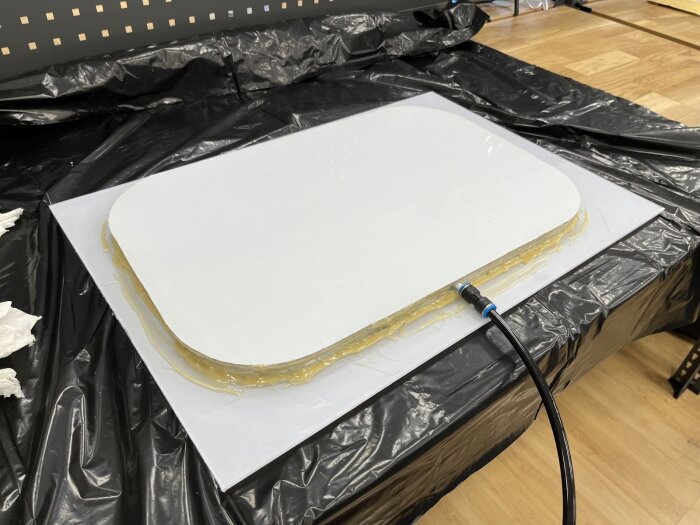 Fönster av polykarbonat med limmade kanter, trycktestas med en luftslang på ett arbetsbord täckt av svart plast.