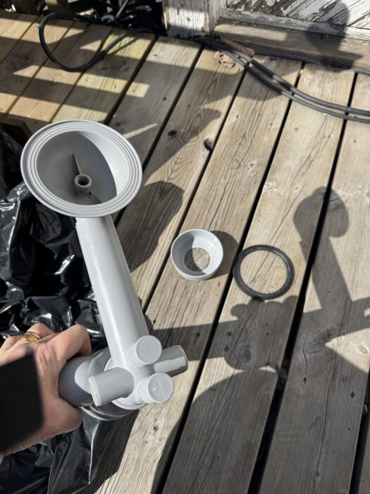 Plaströrsdelar för avloppskoppling i utekök läggs ut på trädäck i solljus.