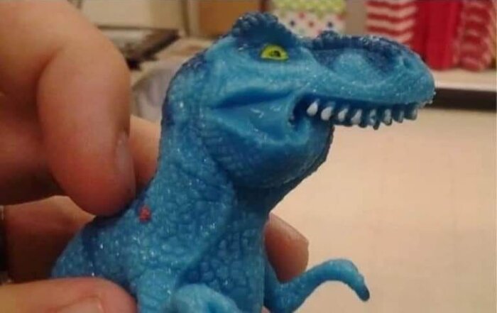 Blå dinosaurieleksak hålls i handen, nästan turkos.