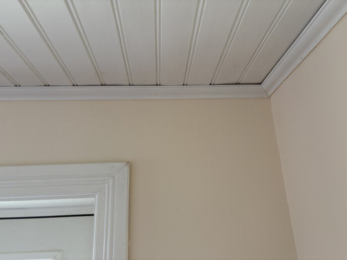 Taklist och dörrkarm mot ljusbeige vägg, fråga om måleriarbete och spackling.