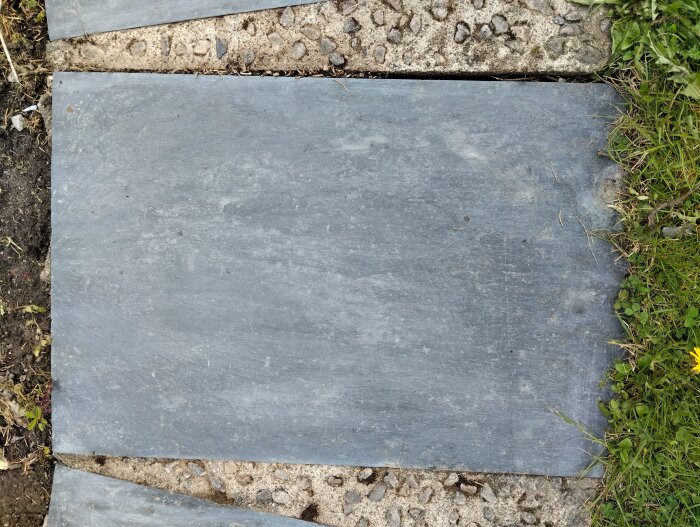 Stålborstad skifferplatta utomhus, omgiven av gräs och jord, visar slät yta efter rengöring.