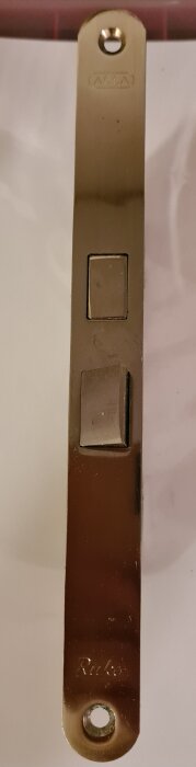ASSA Ruko låskista i metall med hål för montering, sedd uppifrån.