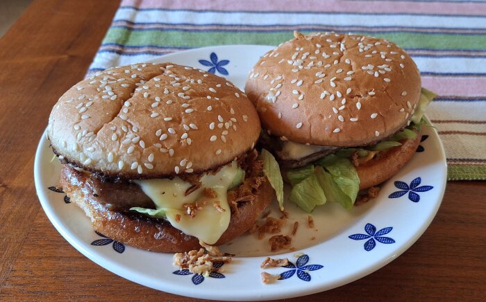 Två hamburgare med ost, sallad och rostad lök på en tallrik, serverade på ett träbord.