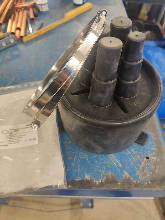 Uponor ändskydd med fyra rör och slangklammer ligger på ett verkstadsbord bredvid en påse med o-ring.