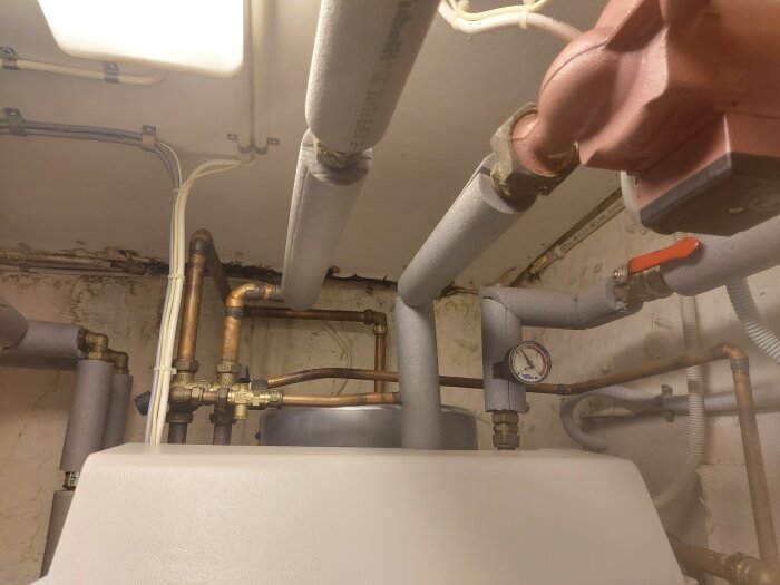 Rör och ventiler i ett värmesystem med isolering och en tryckmätare, troligtvis i samband med en CTC elpatroninstallation.