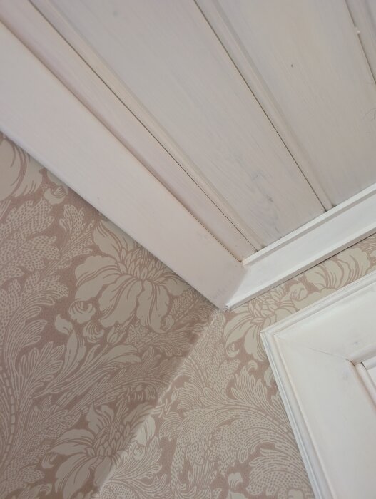 Taklist och slät list möts i ett 90-gradigt hörn med tapetserad vägg och panelluckor i snedtak, delvist täckta med spackel för att passa.