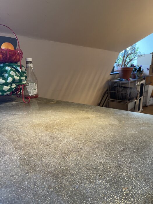 Grovt och slitet betongbänkskiva i kök, med fruktkorg och flaska i bakgrunden; diskuterar renoveringsalternativ för en jämn yta.