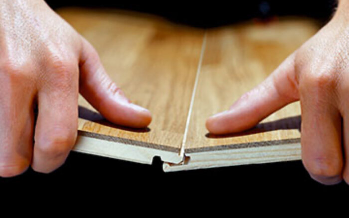 Händer visar två stycken parkettbrädor som sammanfogas med not och fjäder teknik.