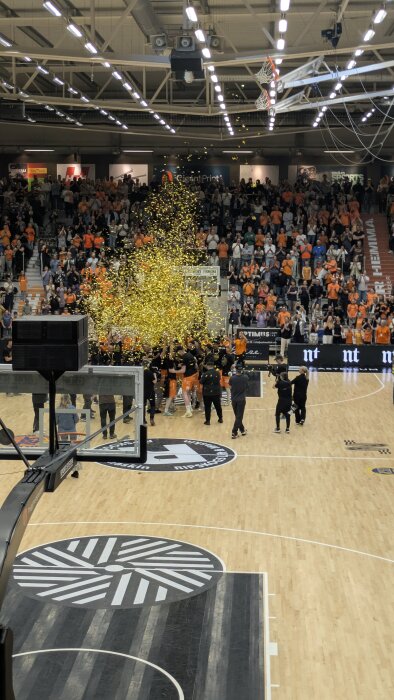Basketlag firar SM-guld i en fullsatt arena med konfettiregn och fans i orange.
