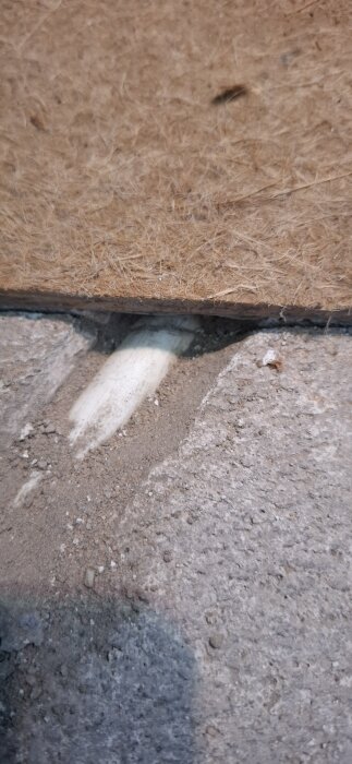 Frilagt rör i marken under en fiberskiva, omgiven av jord och sten, synlig del av byggprojekt.